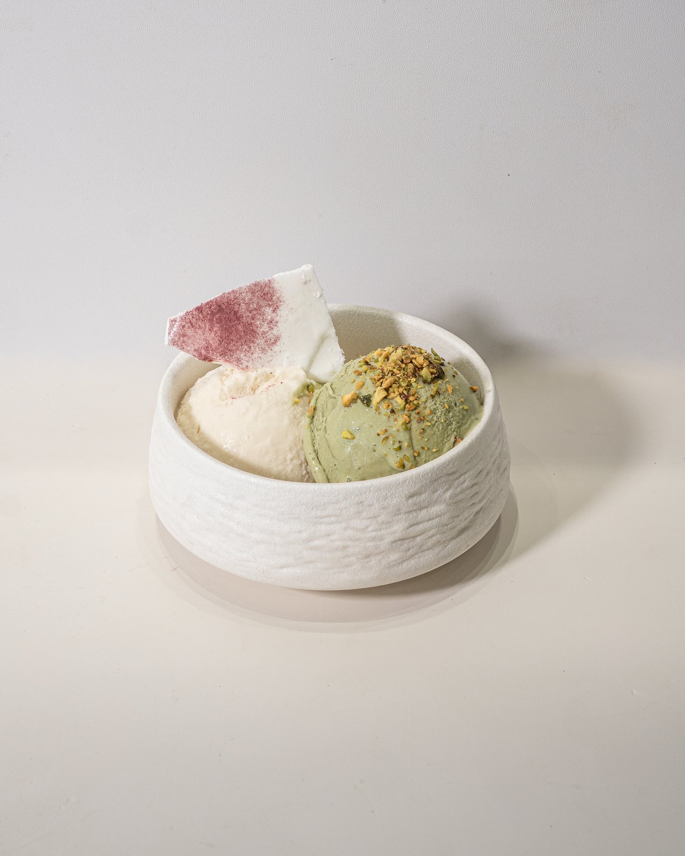 Two scoops of Afrocado gelato, vanilla and pistachio, with a beetroot-dusted meringue shard